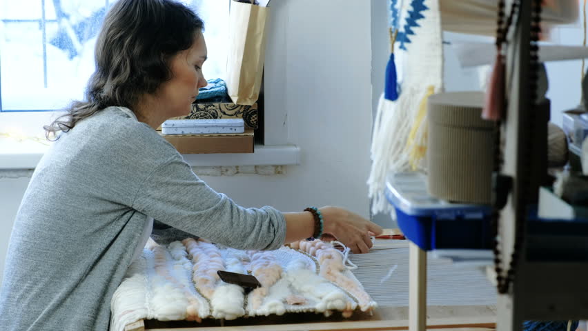 Weaving on a loom. Woman runs the yarn through the threads of the loom with her hands.