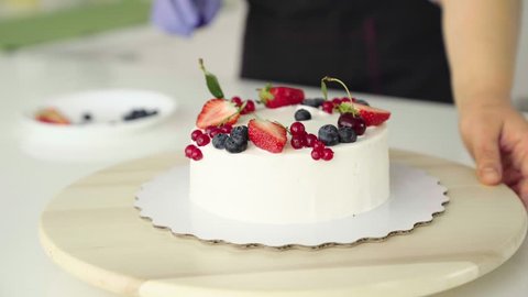 The girl, the chief confectioner, decorates forest berries, strawberries, a homemade cake made from Japanese biscuit. The concept of cooking cakes for restaurants, confectioneries. Copy space
