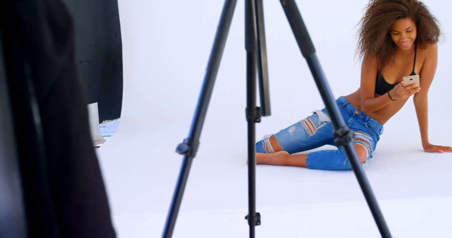 Young African-american model using mobile phone in photo studio 4k