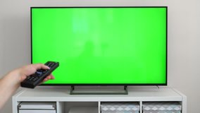 Watching tv with green screen at home interior. Push buttons on remote. Changing channels on television. Closeup on hand with controller
