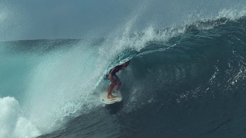 SLOW MOTION, CLOSE UP: Young surfer enjoying the awesome summer by surfing a big emerald wave. Fit male tourist catches a big barrel wave rushing towards the beaches of Tahiti. Extreme water sport.