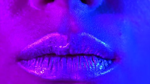 Lips kiss in neon UV lights. Beauty sexy model lips close-up, disco. Woman mouth closeup. Metallic lipstick. Purple and blue ultraviolet lights. Slow motion 4K UHD video