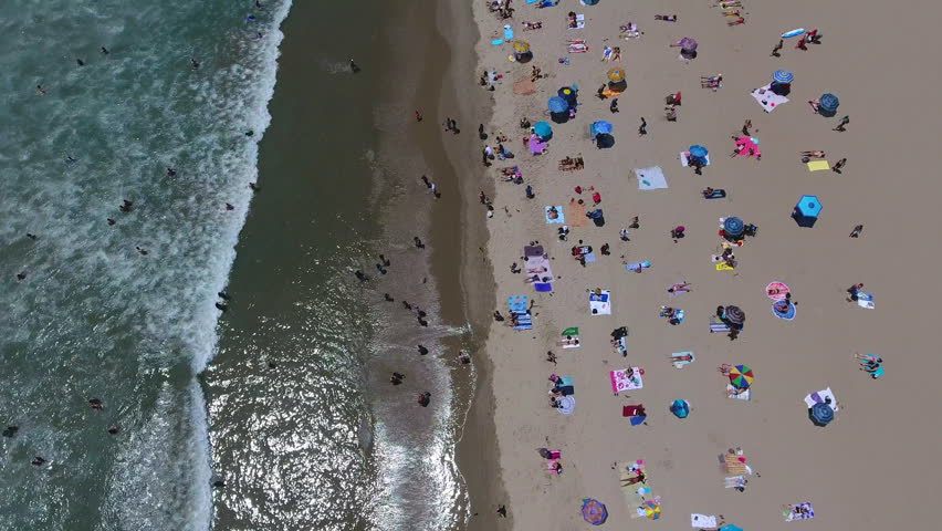 Aerial drone 4K HD of tourists enjoying the summer beach, waves, and sand in Santa Monica, CA. Epic long clip with smooth tilt up to reveal the pier and horizon. For commercials, b-roll, backgrounds.