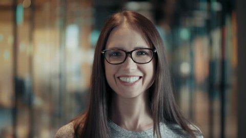 Portrait of attractive smiling young woman in glasses close up face of happy brunette female with long hair in good mood casual team leader or businesswoman in modern start up office positive emotions