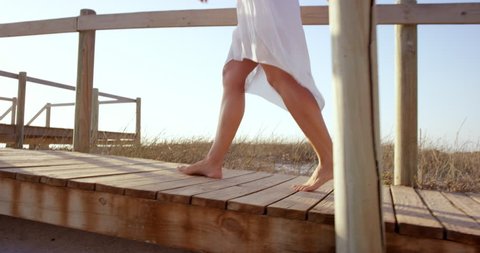 Beautiful woman wearing white dress walking on wooden beach walkway at sunset RED DRAGON