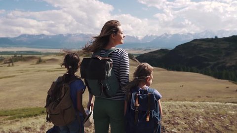 family of tourists on a journey. mother with two daughters in the campaign. children with backpacks admire the view of the mountains