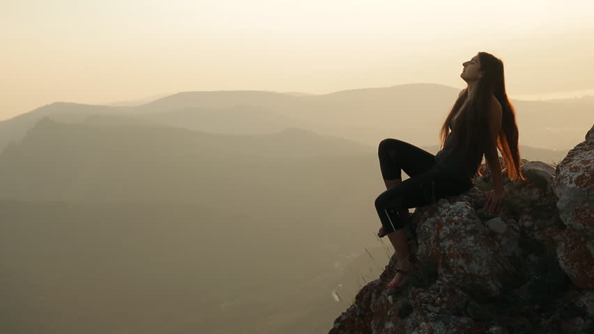 A young woman sitting on top of a mountain.