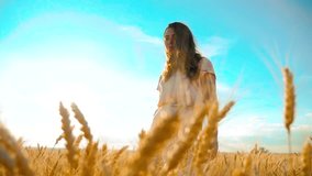 girl is walking along the wheat field nature slow motion video. Beautiful girl in white dress running nature freedom happiness hands lifestyle to the side on field at sunset light and the blue sky