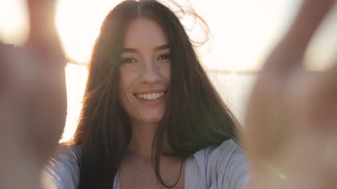 Young smiling woman holding camera make selfie video in sun beams, slow motion
