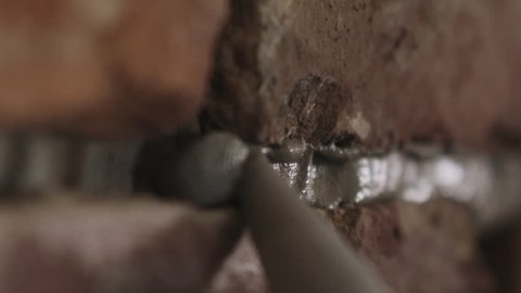 Slow motion handheld closeup of worker filling seam between bricks with mortar from sealant gun