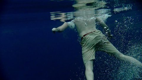 Young man swims underwater in the clear blue lake