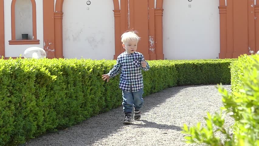 Prague, Czech Republic - May 7, 2018: A boy of two years is playing in the garden of the park. A blond boy runs around the garden. Slow motion