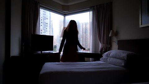 Woman feel sick, come and lay down on bed in suit and skirt, dark bedroom, bright city buildings seen outdoors through window glass. Long haired lady become unwell or sad, rest alone at dim room