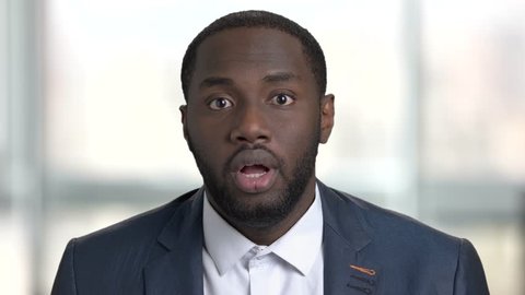 Portrait of shocked afro american business man. Surprised and shocked face of black man in suit, close up. Bright office, windows background.