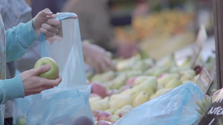 Slow Motion Shot Of Male And Female Customers Hands Choosing Green Apples And Bagging Them Into Blue Plastic Bags At A Street Fruit Market Stall, Supplying Plastic Carrying Bags To Customers. Royalty-Free Stock Footage #1013667485