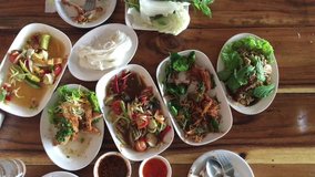 Top view shot eating of Thai food table: Eating north eastern foods (SOM TUM - Spicy Papaya Salad, Sticky rice, Grilled pork salad on wooden table. Local and traditional way. 4K video footage 