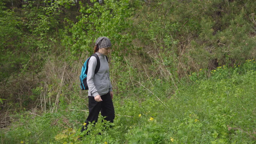 woman with a backpack rises a hill in the forest.