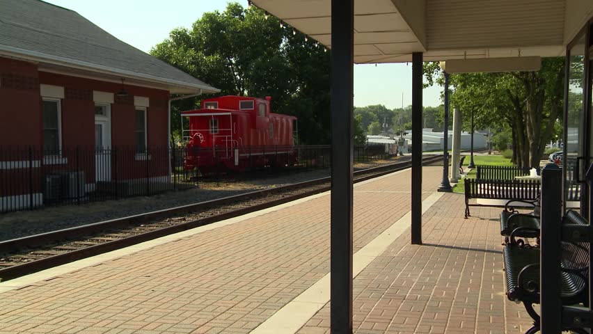A platform for passengers waiting to board trains at a small town rail road depot with an old red caboose for nostalgia.
