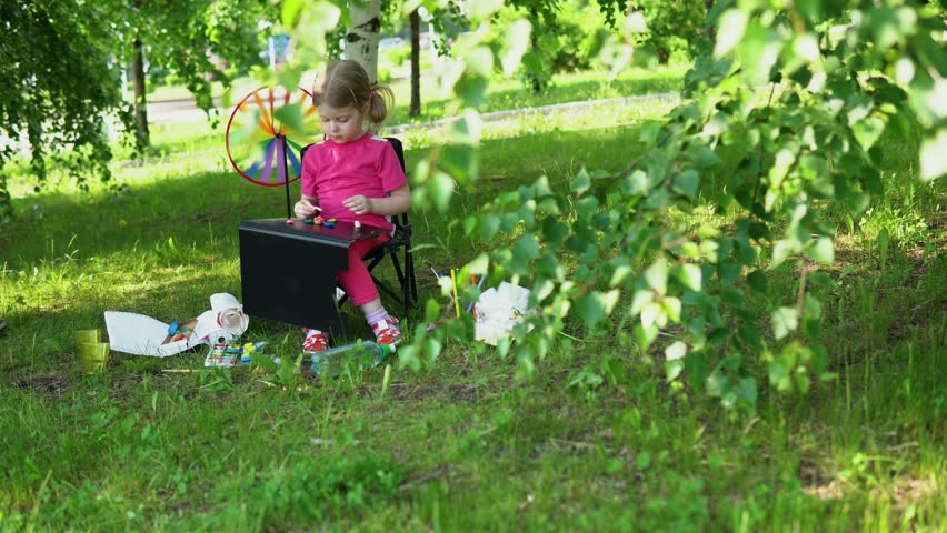 Portrait of little girl sculpts of plasticine in the park. Cute blonde child is engaged in creativity outdoor. Having fun on a summer vacation, holiday concept.
