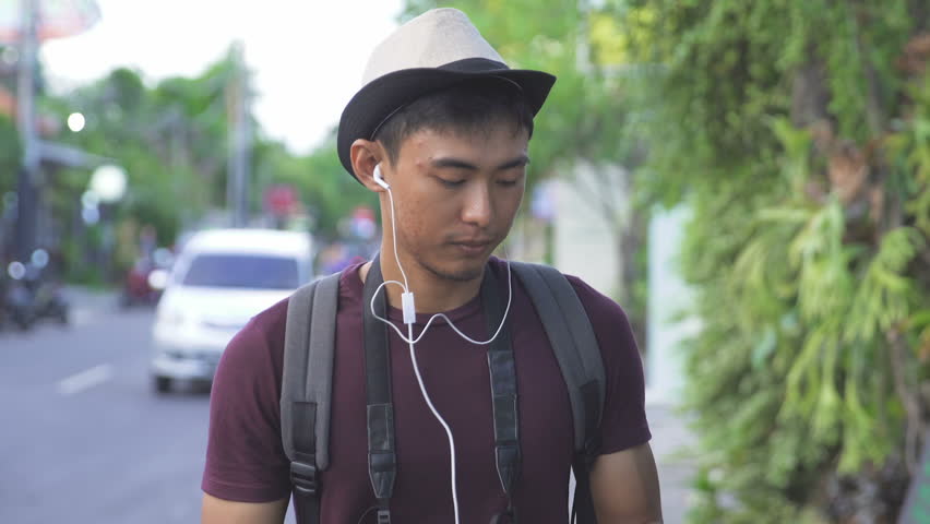 footage of asian young traveller enjoy listening music while walking down the street during summer vacation