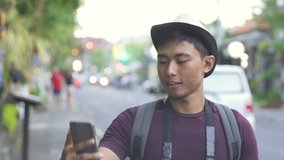 footage of asian traveller video calling with his friends on mobilephone while walking down the street during summer holiday