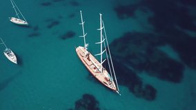 Aerial view of a beautiful sailing boat and other small boats on an emerald and transparent Mediterranean sea. Gulf of the Great Pevero, Emerald Coast (Costa Smeralda), Sardinia, Italy.