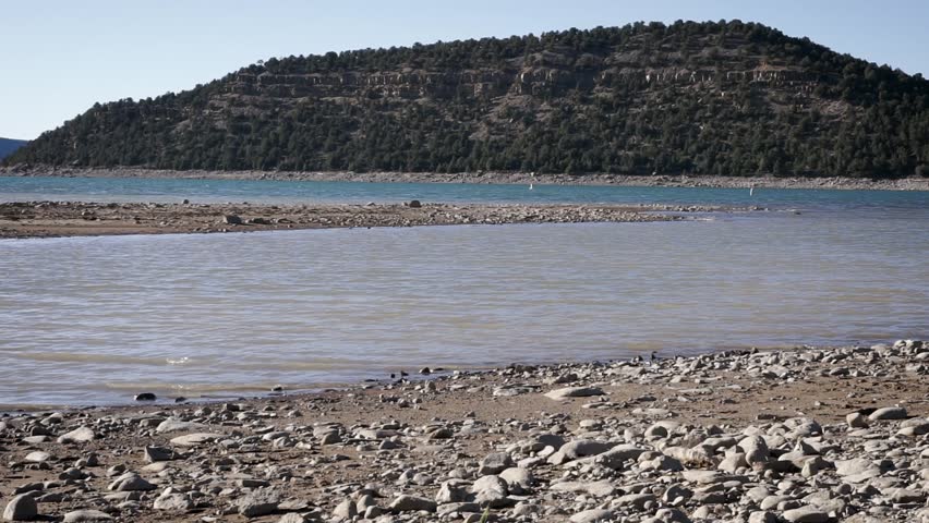 Low Pan Right across rocky beach of a Colorado Mountain Lake Towards two fishing kayaks and a stunt kayak on the shore.