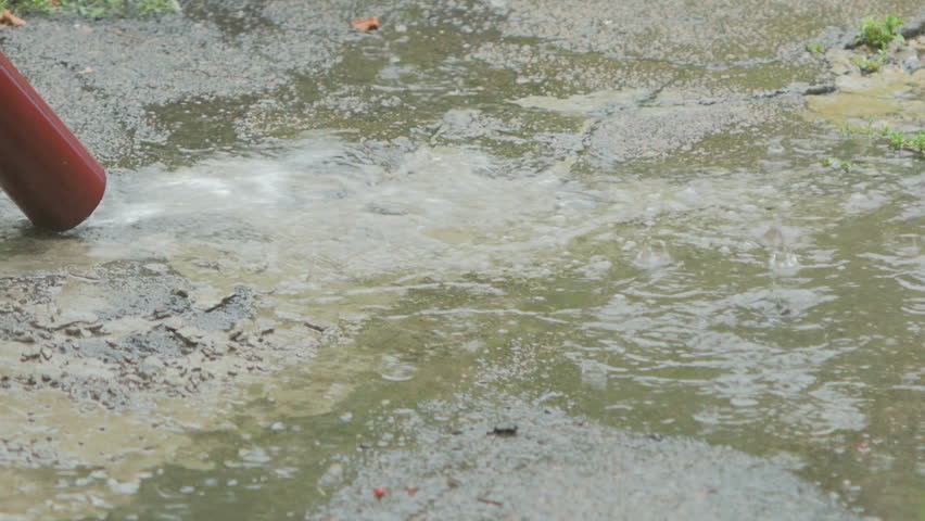 Water flows from the drain pipe to the ground during a heavy rainfall