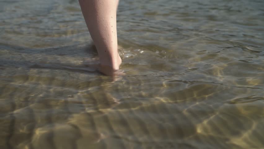 Legs of the girl go on the edge of the shore of the pond.