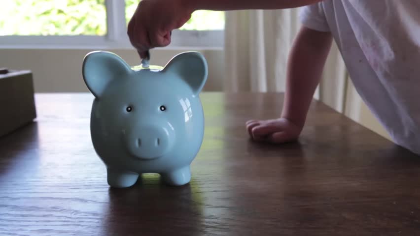 close up footage of a youg childs hand putting money into a blue piggy bank