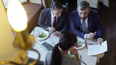 High angle view of three colleagues discussing contract when sitting at table in cafe or restaurant and having business lunch