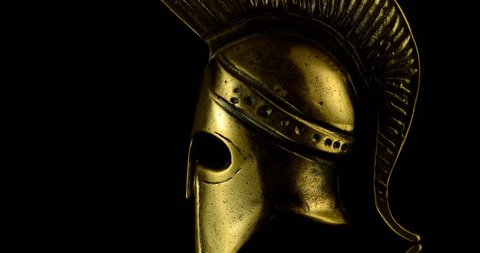 A wonderful golden spartan helmet as part of the equipment of ancient Greek soldiers. King Leonidas and his 300th The piece of metal turns against a black background, shiny and mystical.