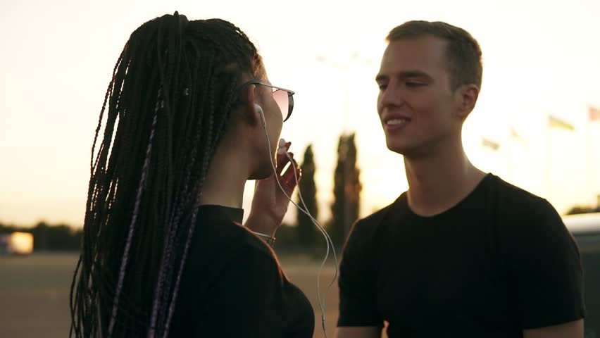 Carefree, joyful young people hanging out together. Listening to the music together with earphones, dancing. Styilish girl with dreadlocks and sunglasses seductivly dancing againt her boyfriend. Close