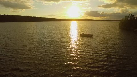 An aerial shot of a couple fishing in the Canadian wilderness on a vast lake by themselves at sunset as the drone pulls away.