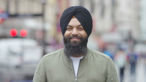 Portrait of young Indian male wearing a turban and smiling to camera, in slow motion