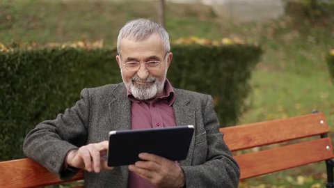 Grandpa use a tablet sitting in the park on the bench