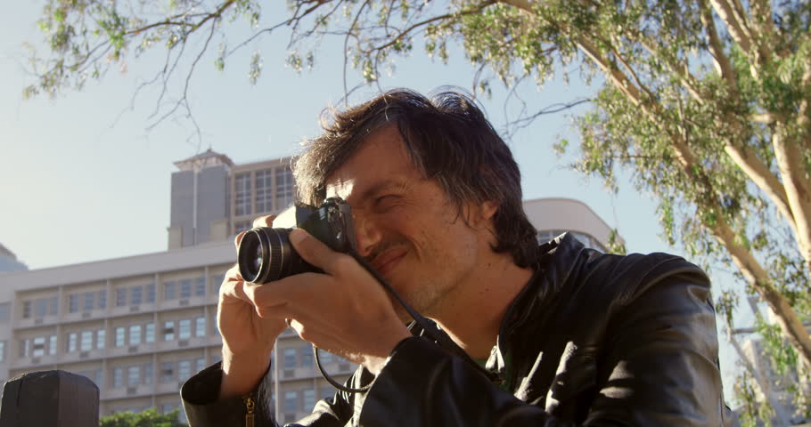 Male photographer taking photos in city street on a sunny day 4k