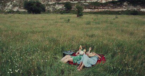 Two girls laying down on the blanket in the middle of nature and throwing up the hats.