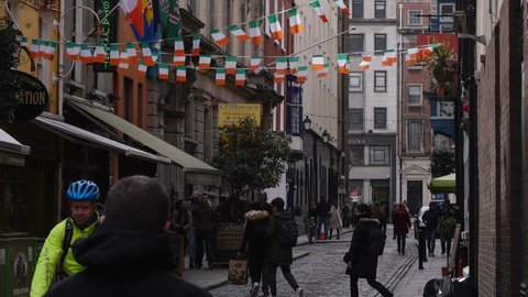 Dublin, Ireland - April 10th 2016: Irish flags fly above cobbled back street in Temple Bar area, Dublin, Ireland. People walk by