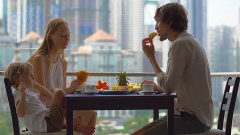 Young family having a breakfast, lunch on their balcony in a skyscraper with a view on a whole downtown of the city