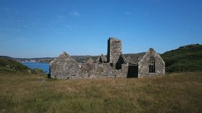aerial video pans over megalithic friary built in 1449, Sherkin Island, Co Cork Ireland. Video passes over building to reveal mouth of harbor, cliff face and small fishing village of Baltimore.