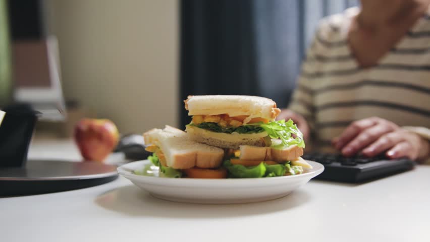 Woman eating sandwich while working. Sandwich from fresh toast with cheese and salad on work place. Work lunch