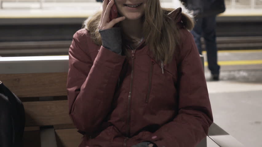 Teenage girl talking on cellphone while waiting for train at night
