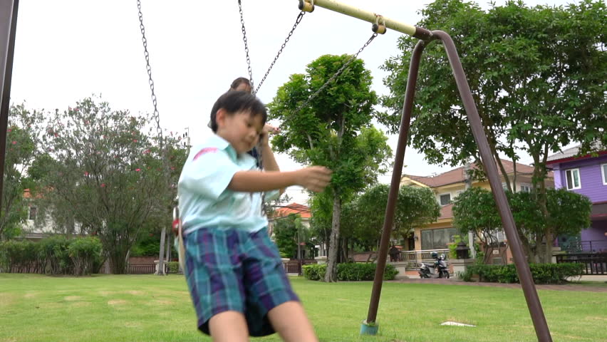 Slow Motion of Funny Asian little kids brother and sister sibling playing swing on the playground at the green park in uniform school.