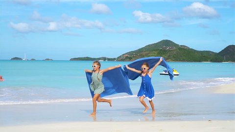 Cute little girls having fun running with towel and enjoying vacation on tropical beach with white sand and turquoise ocean water