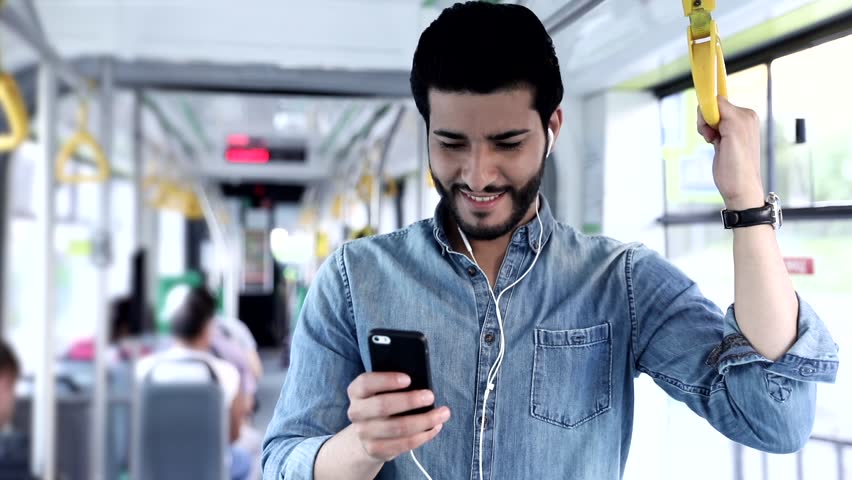 Close up view of Handsome Man Standing on the Public Transport. Interior of Crowded Tram. Man Types on his Mobile Phone. Listening to Music with his Headphones. Luxurious Wristwatch. Casual Clothing. Royalty-Free Stock Footage #1013754590