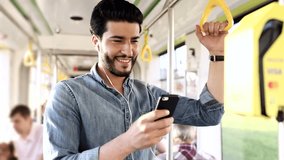 Young Bearded Man Smiling Happily While Chatting on his Smartphone. Standing in the Tram. Holding the Handrails. Sltylishly Dressed. Luxurious Watch on his Wrist. Neat Hairstyle.