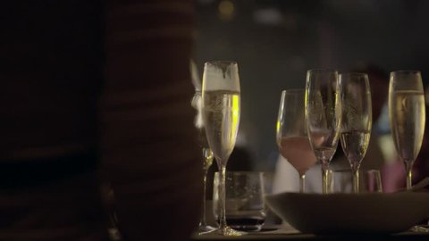 Waiter served champagne glasses on a tray in a fine dining restaurant during concert with bright spotlights in the background.