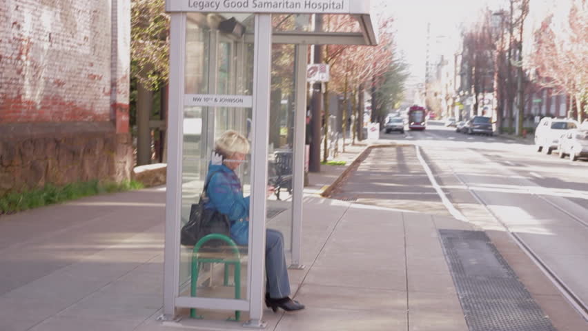 Older blonde woman holding an tablet stands up and approaches an incoming street car in downtown Portland, Oregon