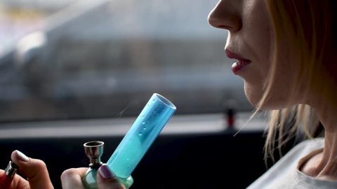 A woman smokes marijuana. The use of hashish through a bong in the car.
